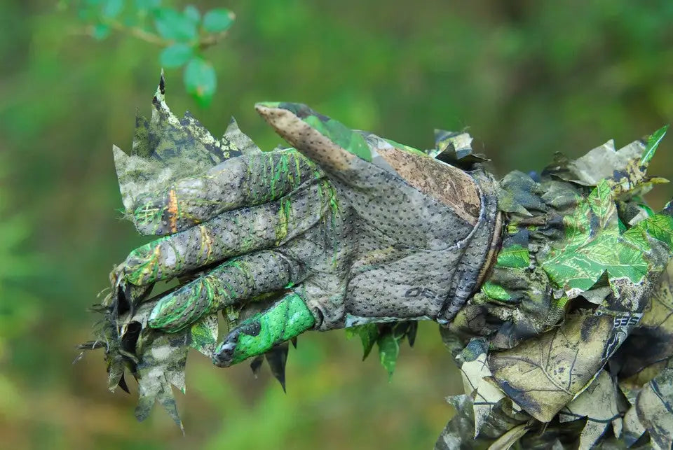 A camouflage-patterned glove with green, brown, and black leaf-like textures, designed for blending into natural environments.