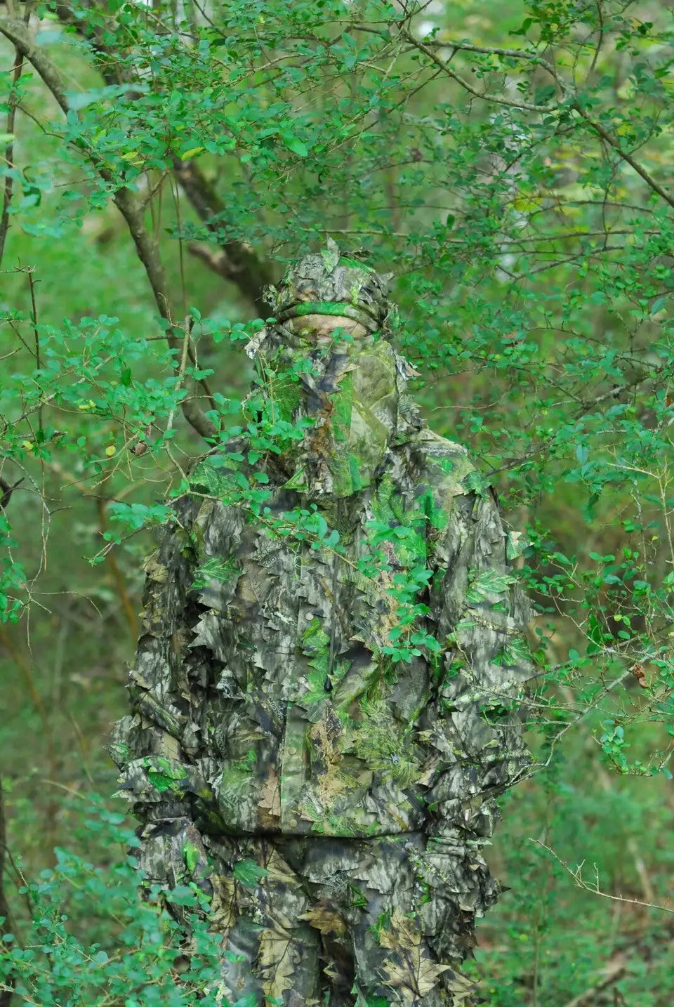 A full-body camouflage suit with leafy green, brown, and gray patterns designed to blend into dense forest environments.