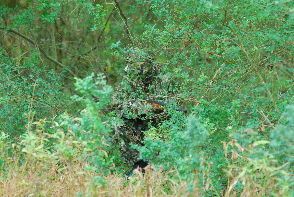 Hunter concealed in green foliage wearing Mossy Oak Obsession